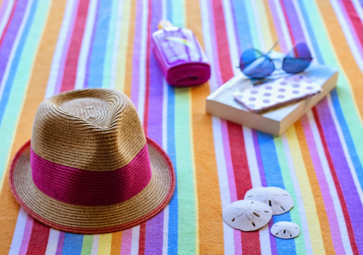 brightly colored beach towel with hat, sunglasses, book, and other accesories on top of it