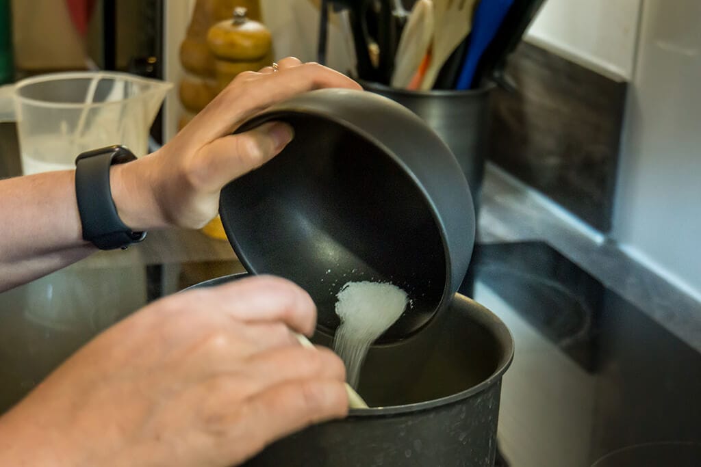 pouring sugar into pot on stove