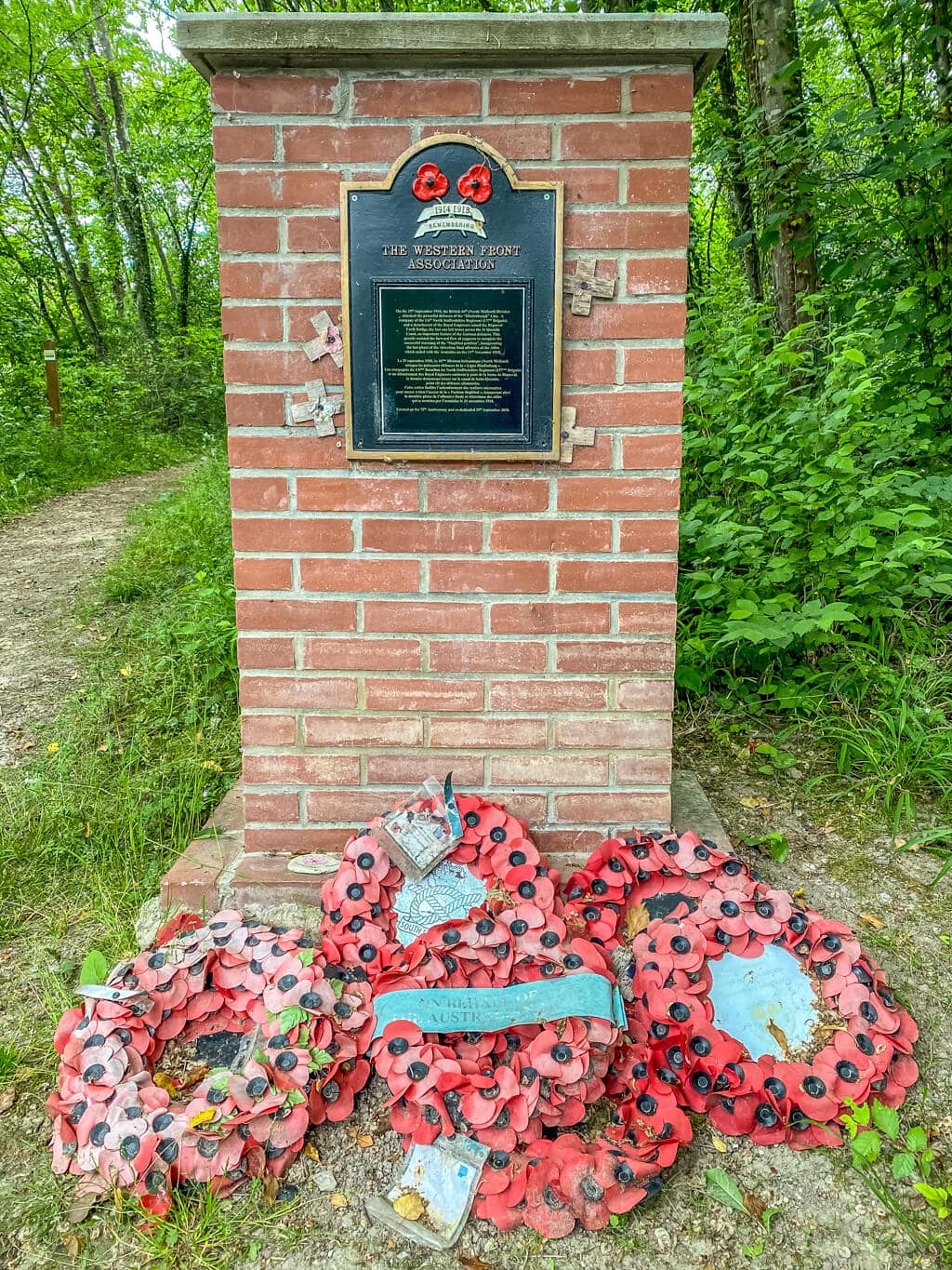 red brick memorial with plaque but words are too small to be read, there are wreaths of poppies in front of it.