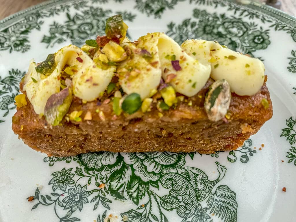 small piece of carrot cake topped with a ribbon of white frosting and pistachios