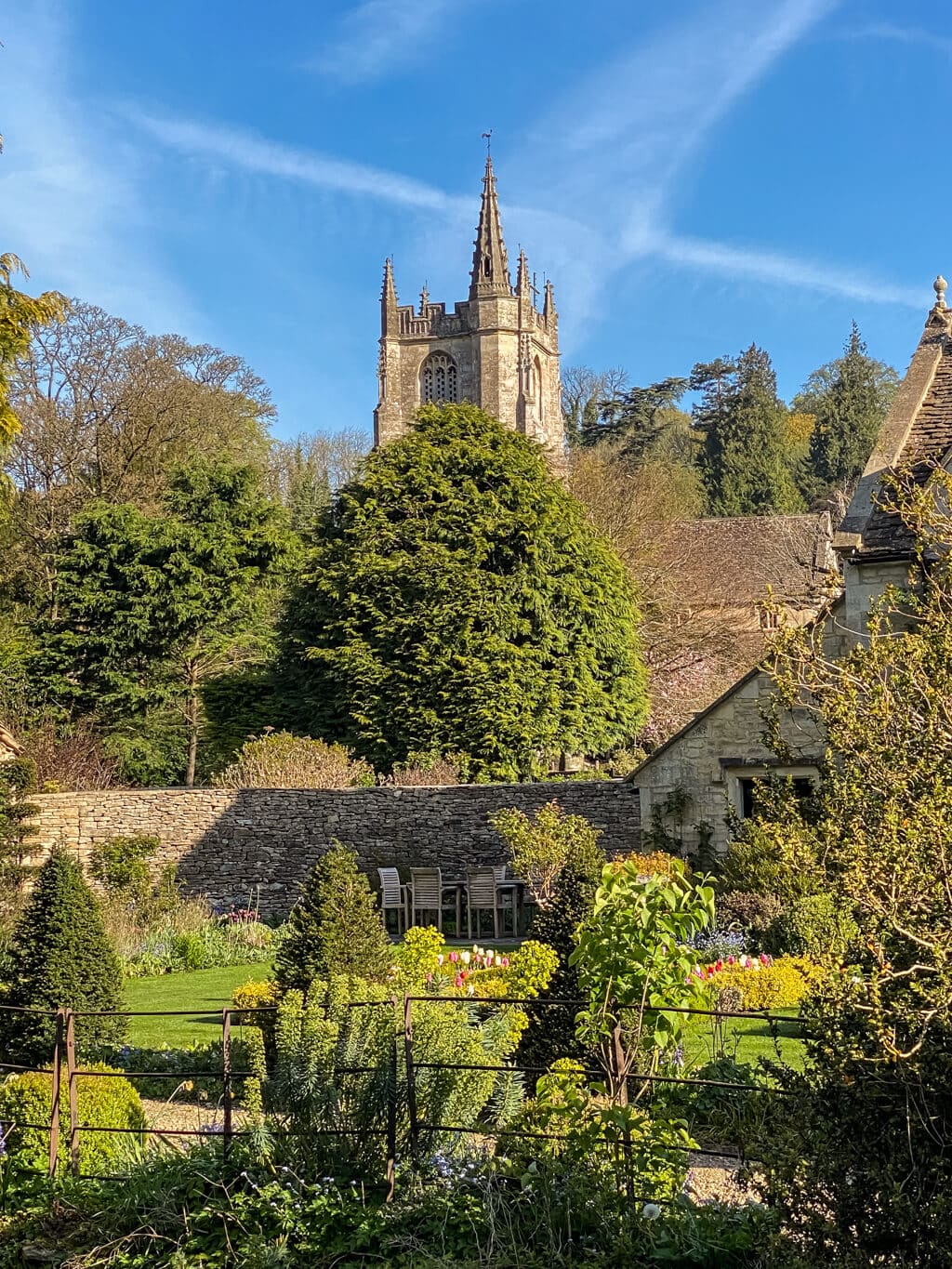 view of the tower of St Andrews church in castle combe with bushes and trees in front